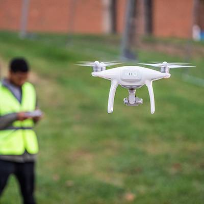 Drone in air Drone flies with student controlling it in the background